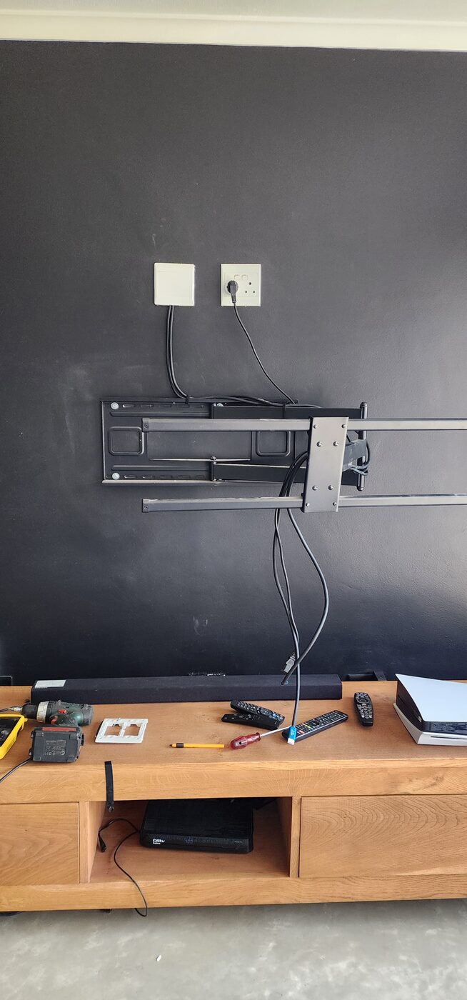 Full-motion TV bracket installed on a wall with a DStv decoder on the media console below